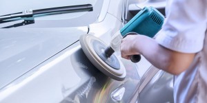 Close up of worker hands using auto polisher to polish a silver car body in the workshop